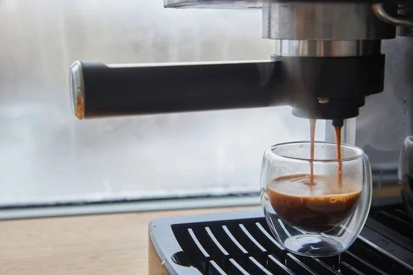 Making fresh coffee going out from a coffee espresso machine. Making espresso in glass transparent coffee cup.
