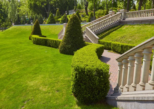 公园背景上的楼梯上有石栏杆 栏杆和铁灯 有豪华的景观设计步行路径 可以走 有绿色的草坪和各种灌木丛 — 图库照片