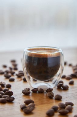 Şeffaf bir fincanda Espresso, ahşap bir masanın üzerinde duruyor, arka planda kahve çekirdekleri ile çevrili.