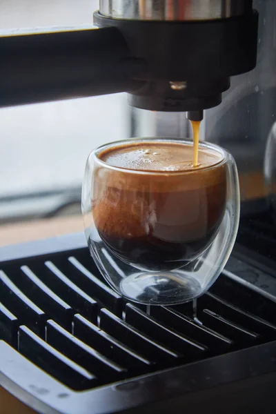 Making fresh coffee going out from a coffee espresso machine. Making espresso in glass transparent coffee cup.