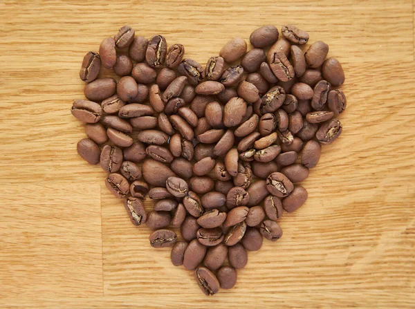 茶色の木製のテーブルの上にハート型の黒いコーヒー豆の種 ダークコーヒーアラビカロバストなロースト穀物の風味の香りのカフェ 自然コーヒーショップの背景 上から近いビュー コピースペース ロイヤリティフリーのストック画像