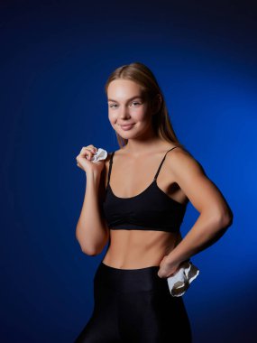 Kafkasyalı, eşofmanlı, havluyla gülümseyen, koyu mavi duvarlı bir kadının resmi.