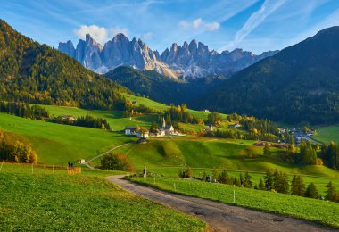 Santa Maddalena köyünde muhteşem bir sonbahar manzarası var. Kilise, renkli ağaçlar ve yükselen güneş ışınları altında çayırlar. Dolomite Alpleri, Güney Tyrol, İtalya.
