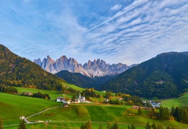 Santa Maddalena köyünde muhteşem bir sonbahar manzarası var. Kilise, renkli ağaçlar ve yükselen güneş ışınları altında çayırlar. Dolomite Alpleri, Güney Tyrol, İtalya.