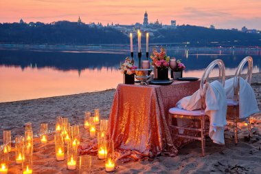 Nehir kıyısında bir randevu, süslü bir masa aşık bir çifti bekliyor. Arka planda şehir ışıkları, akşam Kyiv, Ukrayna.