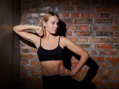 Spor ve yoga yaşam tarzı konsepti. Spor kıyafetli genç bir kadın kırmızı tuğla duvara karşı poz veriyor..