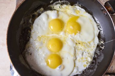 Four eggs are fried in a black pan on the gas stove