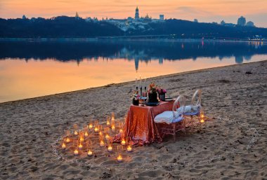 Nehir kıyısında bir randevu, süslü bir masa aşık bir çifti bekliyor. Arka planda şehir ışıkları, akşam Kyiv, Ukrayna.