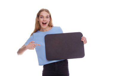 Smiling young woman holding empty signboard with copy space and pointing at her. Concept of positive social awareness.
