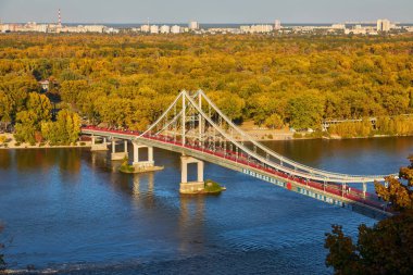 Sonbaharda Kyiv 'in sağ kıyısında, Ukrayna' da ve sıcak bir sonbahar gününde insanların yürüdüğü Dnipro Nehri üzerindeki yaya köprüsünün manzarası.