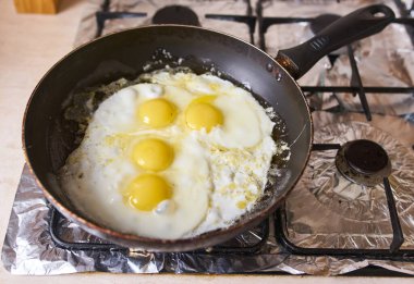 Four eggs are fried in a black pan on the gas stove