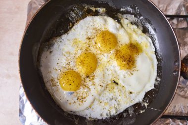Four eggs are fried in a black pan on the gas stove