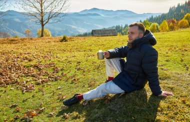 Bir turist, güzel sonbahar dağlarının ve doğanın arka planında kahve içer.
