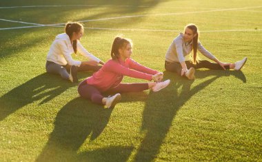 Futbol stadyumunda esneme egzersizleri yapan üç kız.