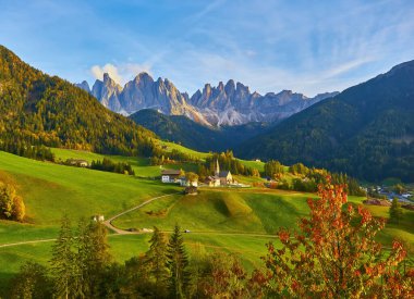 Santa Maddalena köyünde muhteşem bir sonbahar manzarası var. Kilise, renkli ağaçlar ve yükselen güneş ışınları altında çayırlar. Dolomite Alpleri, Güney Tyrol, İtalya.