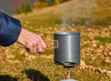 Bir adamın eli, dağların arka planında yemek yemek için bir kap tutuyor, bir fast food sistemi, güvenli bir gaz ocağı, yürüyüş ekipmanları, yürüyüş aletleri. Yüksek kalite fotoğraf