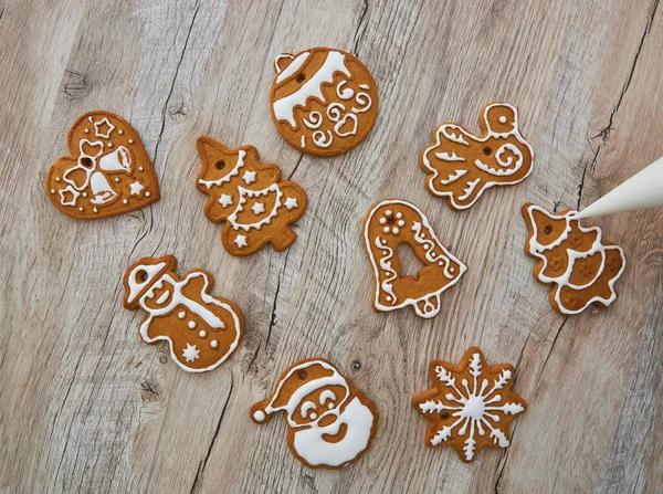 Close up of drawing gingerbread Christmas snowflake sugar cookie on wooden table background with white icing, concept of holiday celebration.