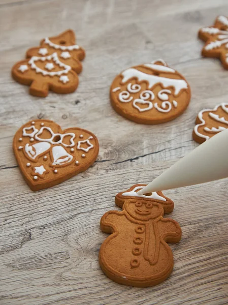 Close up of drawing gingerbread Christmas snowflake sugar cookie on wooden table background with white icing, concept of holiday celebration.