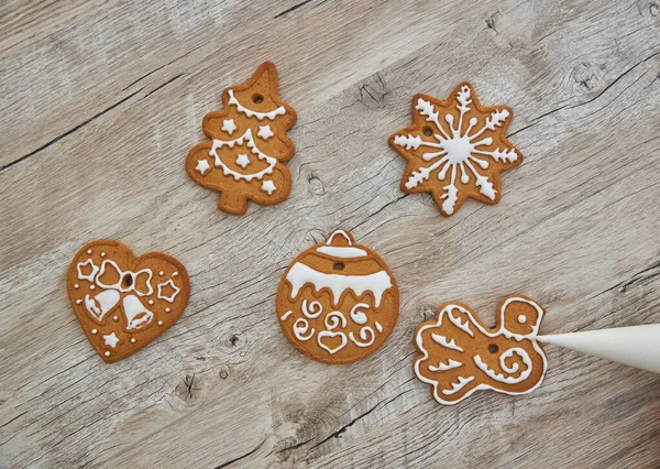 Close up of drawing gingerbread Christmas snowflake sugar cookie on wooden table background with white icing, concept of holiday celebration.