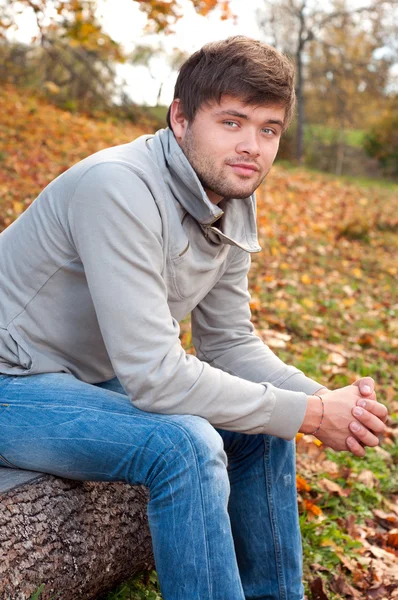 Ao ar livre retrato de jovem feliz sentado no parque de outono — Fotografia de Stock