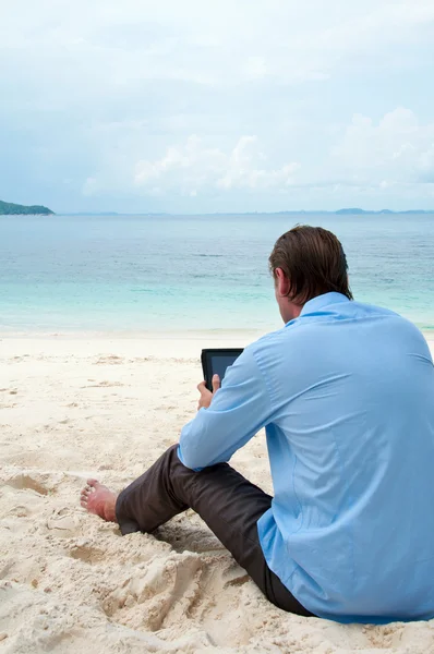 Ο άνθρωπος κάθεται και εργάζεται στην παραλία με δισκίο comput των επιχειρήσεων — Φωτογραφία Αρχείου