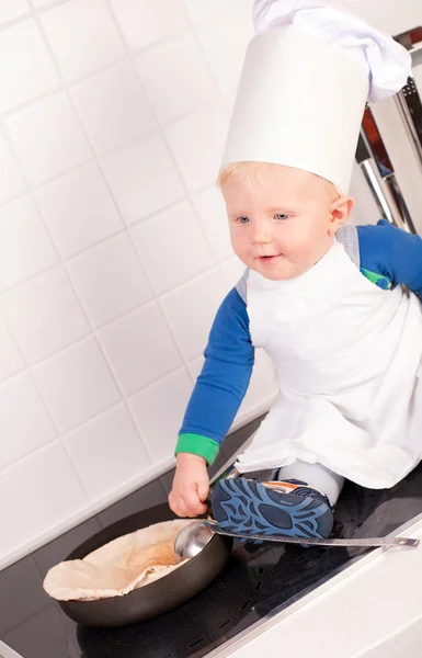 Kleine baby chef-kok in de hoed van de kok maken de pannenkoeken — Stockfoto