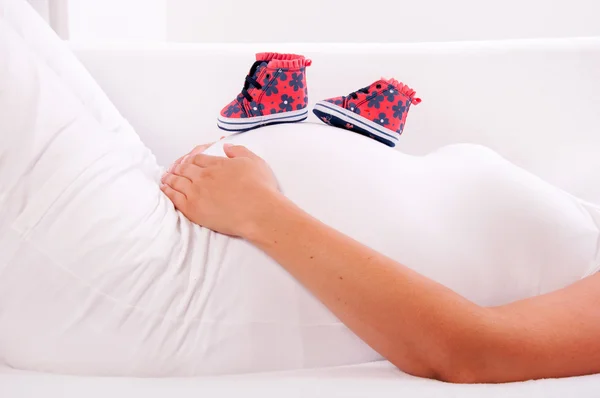 Sapatos pequenos para o bebê por nascer na barriga da mulher grávida — Fotografia de Stock