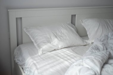 Pencereden sabah ışığı beyaz saten bir yatağın üzerine düşüyor. İyi ve sağlıklı uyku kavramı.