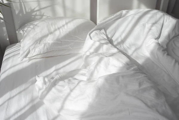 白いサテンの寝具とベッドの上に落ちる窓からの朝の光 — ストック写真