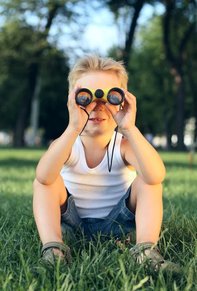 En liten gutt sitter i parken med en kikkert. – stockfoto