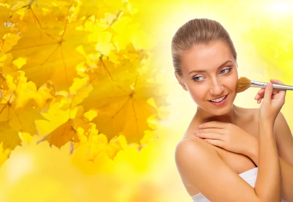 Young woman with makeup brush on autumnal background — Stock Photo, Image