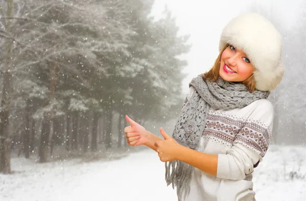 Молодая девушка показывает хорошо жест в снежном лесу — стоковое фото