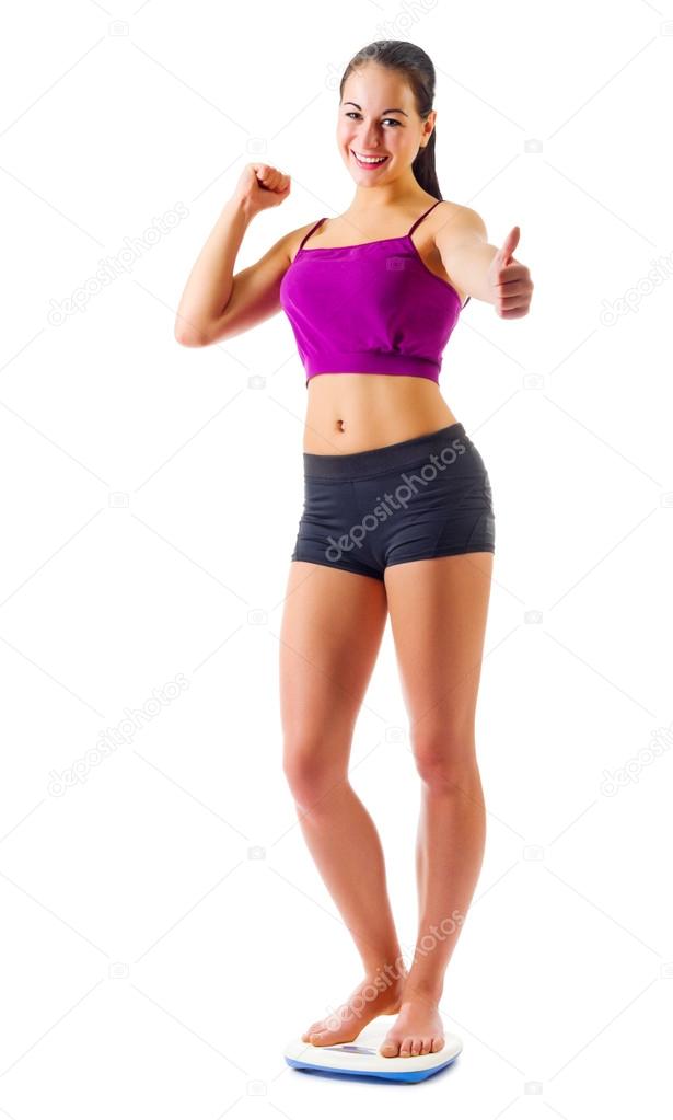 Young sporty girl on scales shows ok gesture