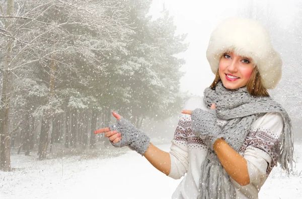 Young woman in fur hat shows pointing gesture at forest — Stock Photo, Image