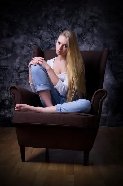 Young girl sit in chair on grey wall background — Stock Photo, Image