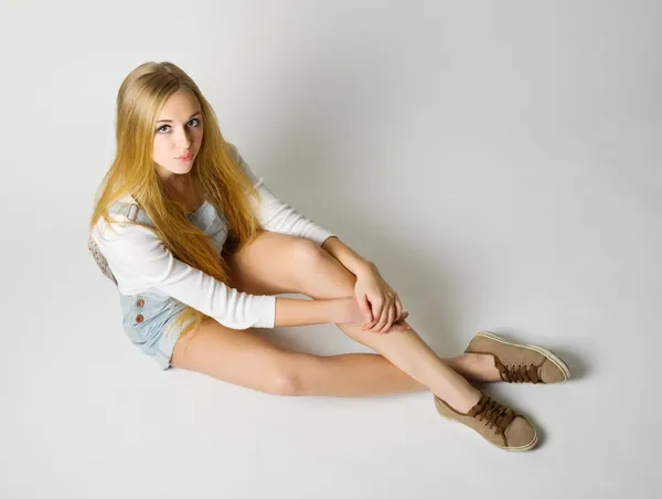 Молодая девушка сидит на полу на сером — стоковое фото
