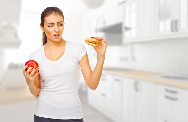 Girl with hamburger and apple ay kitchen — Stock Photo, Image