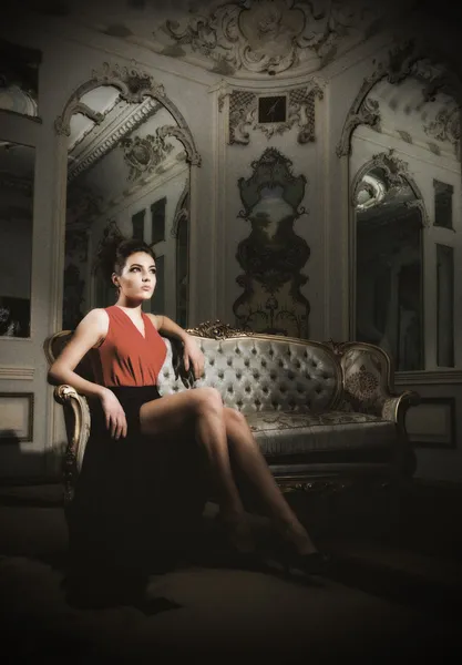 Jeune femme assise sur un canapé dans une chambre ancienne — Photo