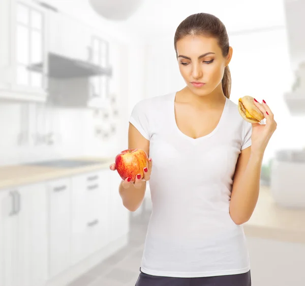 Девушка с яблоком и гамбургером в светлой комнате — стоковое фото