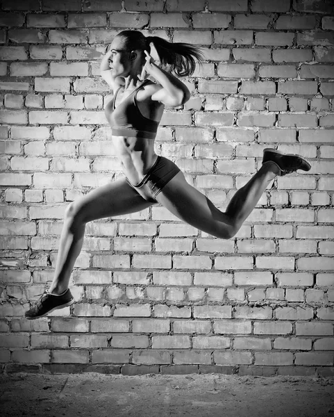 Mujer saltando muscular sobre fondo de pared de ladrillo (ver monocromo ) — Foto de Stock