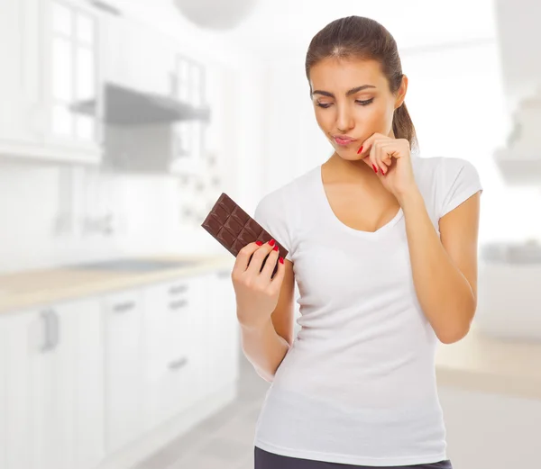 Zweifelnde Frau mit Schokolade in der Küche — Stockfoto