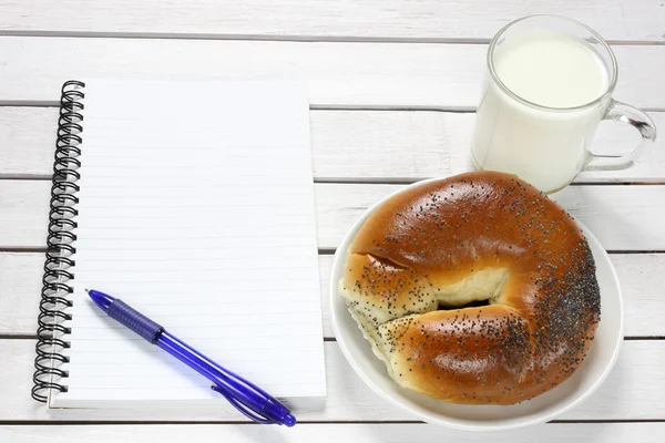 Caderno, croissant e leite na mesa de madeira — Fotografia de Stock