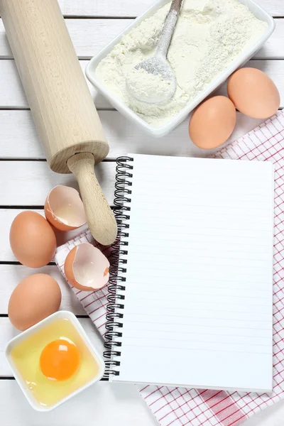 Notebook, eieren, bloem en rolling pin op houten tafel — Stockfoto