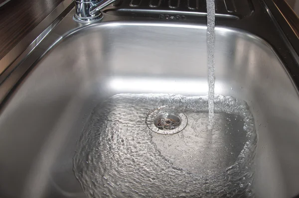 Stainless steel sink plug hole close up with water — Stock Photo, Image