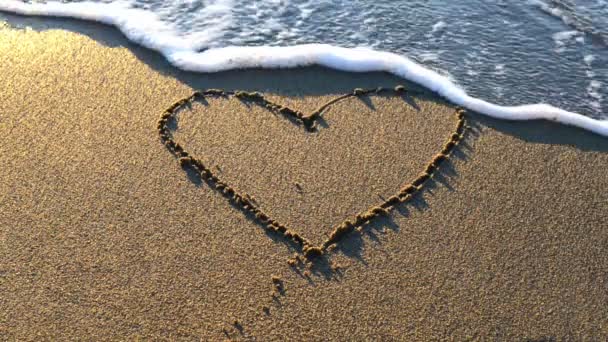 Corazón dibujado en la arena de la playa con espuma de mar y olas — Vídeo de stock