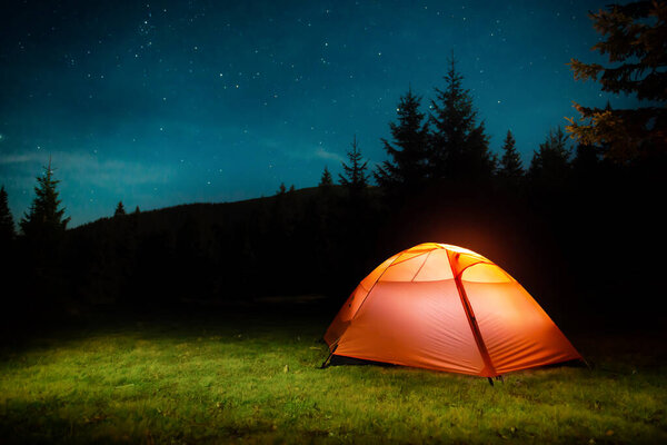 Оранжевая освещенная палатка в темном ночном лесу с ночным небом и звездами