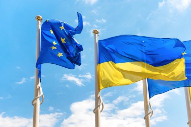 Ukraine and European Union flags on poles fluttering by wind on blue sky. Ukrainian flag