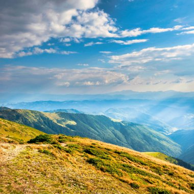 Mountains landscape with peaks, sun, clouds and grass field