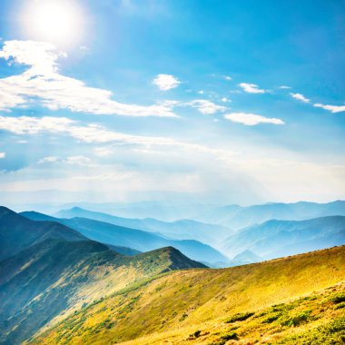 Mountains landscape with peaks, sun, clouds and grass field