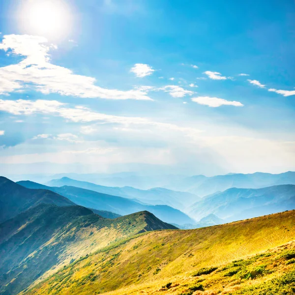 Mountains landscape with peaks, sun, clouds and grass field